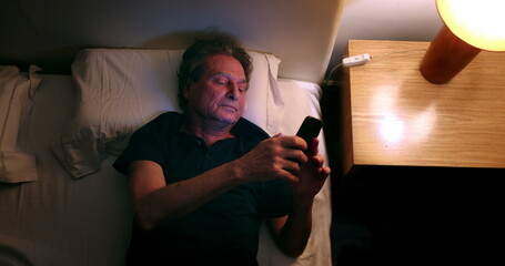 Man turns nightstand light ON and picks up cellphone. Person checking smartphone screen