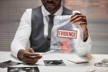 Close up of Black male detective holding plastic bag with evidence during interrogation of suspect,...