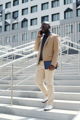 Young confident businessman in formalwear and eyeglasses moving downstairs and talking to client or business partner on smartphone