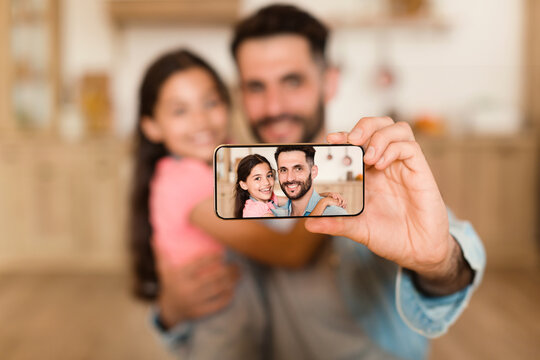 Bonding concept. Happy father taking selfie with his daughter on cellphone, selective focus on device screen