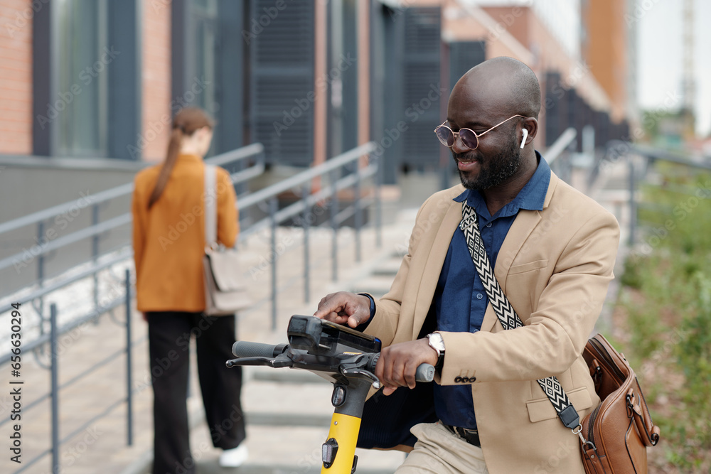 Poster young smiling african american businessman choosing settings on scooter terminal before riding home 