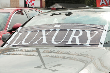 luxury word text sign banner flag on front of black car vehicle windshield at dealership outside exterior on bright day