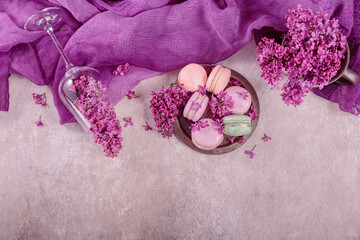 Sweet pastel french macaroons and lilac flowers on light gray background. Beautiful composition for bakery and pastry shop. Top view with copy space
