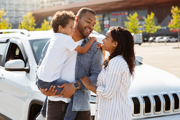 Happy african american family posing outdoors next to new car
