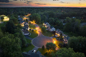 Upscale suburban homes at sunset with large backyards and green grassy lawns. Illuminated private...