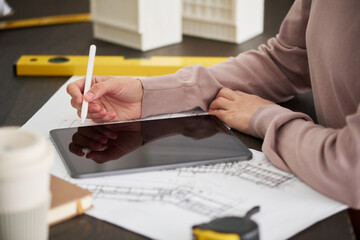 Hand of young female engineer or architect in blue pullover holding stylus over tablet screen while...