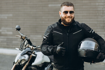 Man biker standing by his motorbike holding his helmet