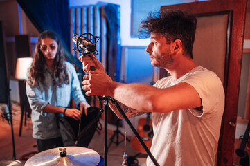 Sound technician setting up a condenser studio microphone above a drum set.