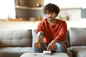 Healthcare Concept. Indian Man Checking Blood Pressure With Modern Tonometer At Home