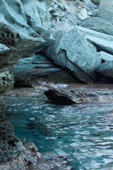 A serene rocky coastal scene on the island of Crete, featuring jagged stone formations and clear turquoise waters. The natural textures and colors capture the untouched beauty of the Mediterranean.