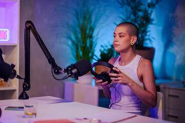 Urban girl is sitting in a home recording studio nd preparing for recording a podcast.
