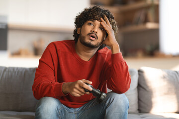 Upset Indian Man With Joystick In Hand Sitting On Couch At Home