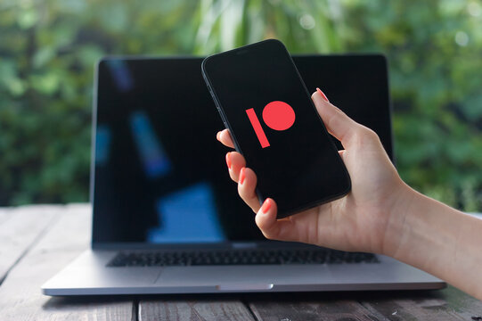Patreon logo, American crowdfunding website, displayed on iPhone screen with MacBook Pro in the background
