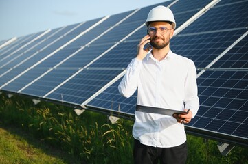 Positive bearded male investor standing against photovoltaic panels producing alternative energy.