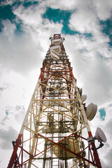 Tall, high and straight telecommunication antenna, made up with white and red metal in front of an expressive light blue and cloudy sky shot in a low angle - obrazy, fototapety, plakaty