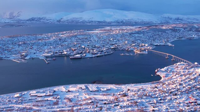 Aerial sunset view of snowy houses, fjord and bridge of Tromso town, Norway. Sunny winter weather