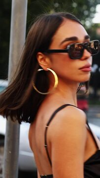 close-up of a beautiful girl in black glasses on in the city against the background of traffic cars. vertical video