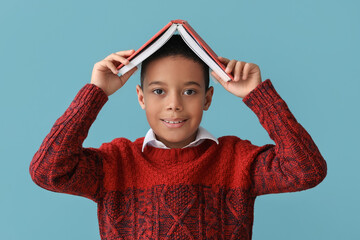 Cute African-American boy in knitted sweater and with book on blue background