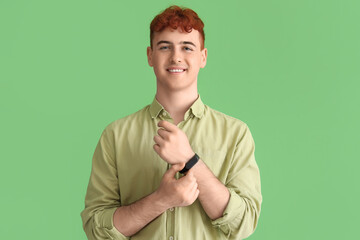 Young redhead man with smartwatch on green background