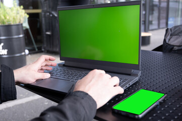 Rear view man freelance working in cafe, using a laptop computer with a green screen on the monitor. Concept remote work, freelance, working on a laptop computer or net-book.