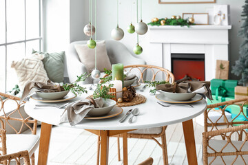 Christmas table setting with hanging balls, burning candles and pine cones in living room