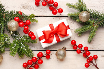 Christmas tree branches with balls, rowan and gift box on white wooden background