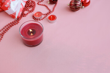 Christmas ornaments, burning candles, beads and gift box with white ribbon bow lie on a pink...
