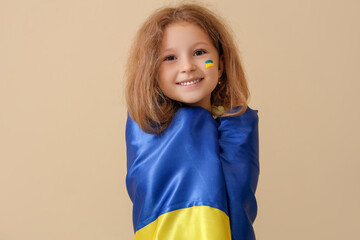 Happy little girl with Ukrainian flag on beige background
