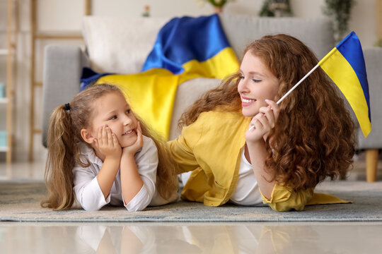 Happy little girl and her mother with Ukrainian flags lying on floor in living room