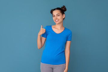 Young woman in t-shirt showing thumb-up on blue background