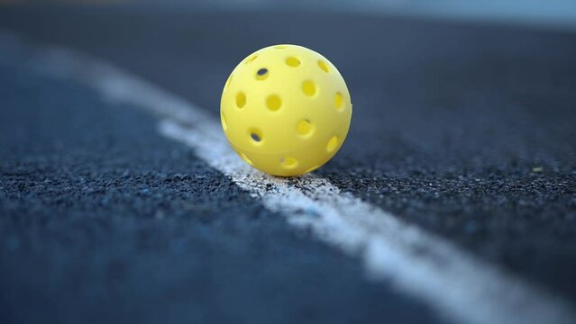 Perforated plastic ball for pickleball rolling on court in slow motion