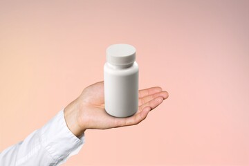Human hand holding white blank bottle. Packaging for supplements.