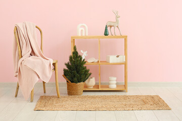 Shelving unit with Christmas decor, small fir tree and armchair near pink wall