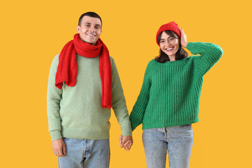 Beautiful young couple in warm clothes on yellow background