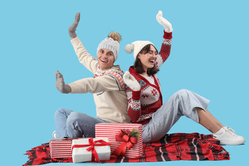 Obraz premium Happy young couple in warm clothes with gift boxes sitting on blue background