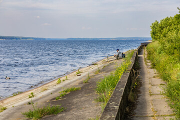 Obraz premium Old fisherman in hat and dark glasses do fishing at the coast of big lake at sunny morning