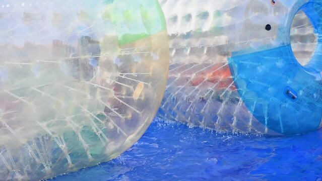 Children running inside blue and green aqua zorbing cylinders at an amusement park