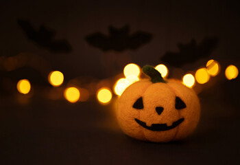 Jack o lantern head and bats on a dark background with bokeh. Cute Halloween pumpkin made of wool.