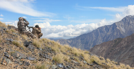Couple of men in camouflage with binoculars and telescope are observing in the high mountains.