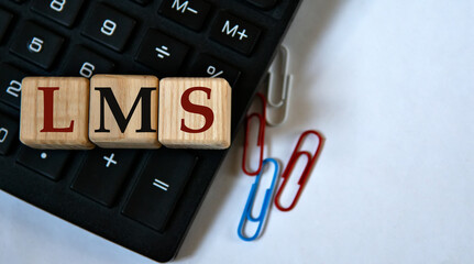 LMS - acronym on wooden cubes against the background of a calculator and paper clips. Copy space