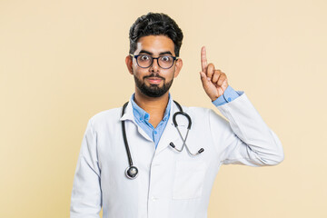 Eureka. Inspired Indian young doctor cardiologist man pointing finger up with open mouth, having...