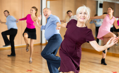 Fototapeta na wymiar Portrait of positive older woman enjoying active dancing during group training in dance studio..