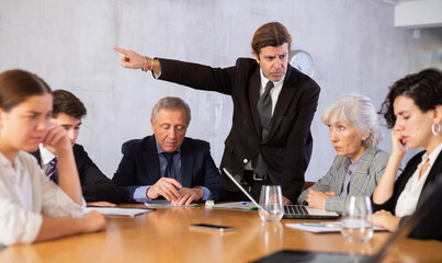 Fototapeta premium Portrait of angry male boss in business suit pointing to the door to his subordinate during a meeting forcing him