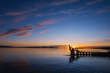 Obraz premium Silhouette of Black rock diving board with people looking at stunning nature sunset scene. Salthill beach, Galway town, Ireland. Rich blue and orange color. Famous city landmark and area. Aerial view.