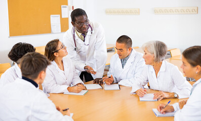African american doctor lecturing to adult audience sitting around same desk during refresher...