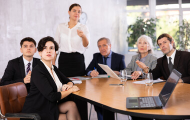 Young adult old office workers sitting at table and looking at screen while young female using projector remote control in meeting room