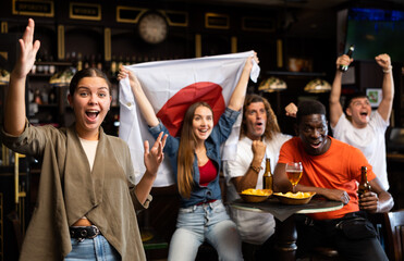 Emotional young female fan watching football match in sports bar, gesturing emotionally, happy with...