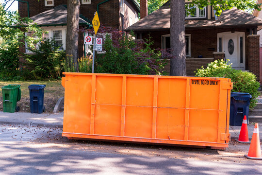 A roll-off construction dumpster parked on a residential street with traffic cones on a shady street in an older neighourhood. shot in toronto in the fall side view from street room for text