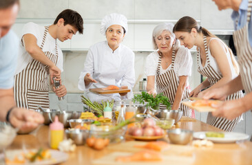 Chef in cook uniform teaches cooking class students how to clean and cut salmon fillet