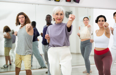 Portrait of smiling determined elderly woman practicing basic punches during group self defense...